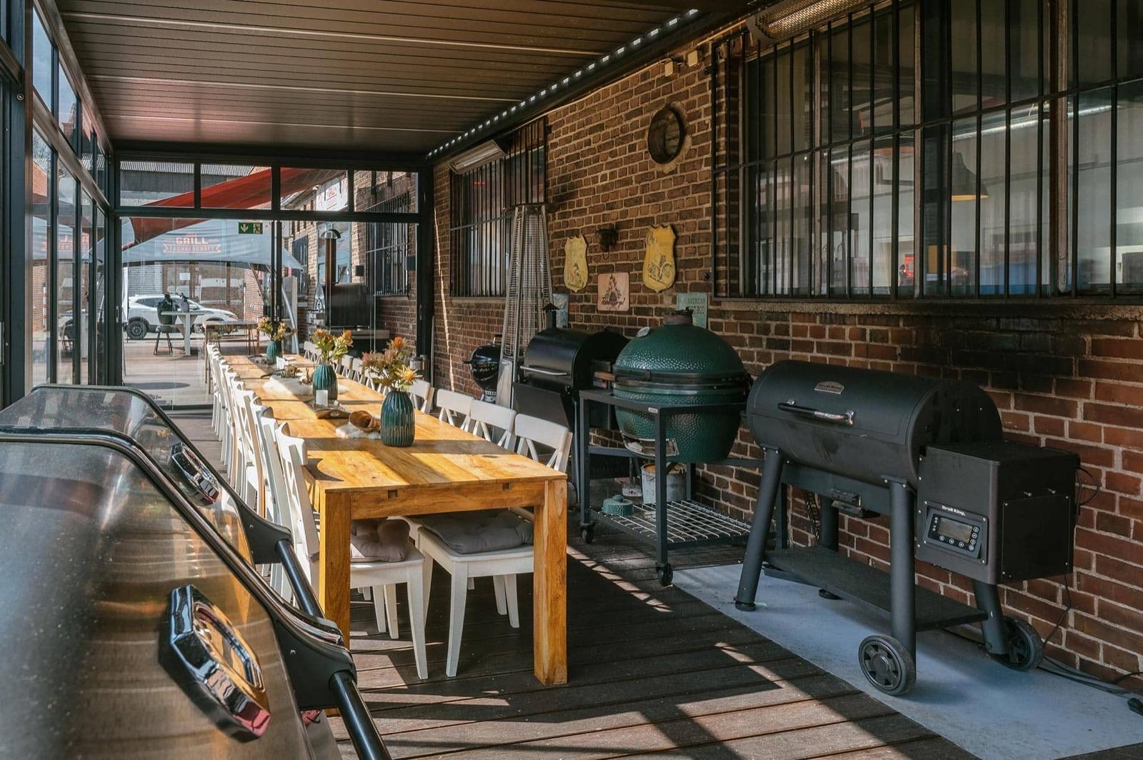 Überdachte Grillterrasse mit großen Grills und gedeckter Holztafel